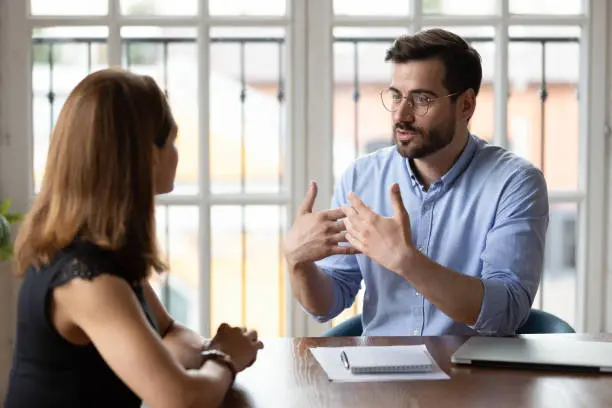 hr-mission Confident male boss leader in eyeglasses explaining project details to new female employee at meeting. Concentrated young woman job applicant listening to hr manager questions at interview in office.